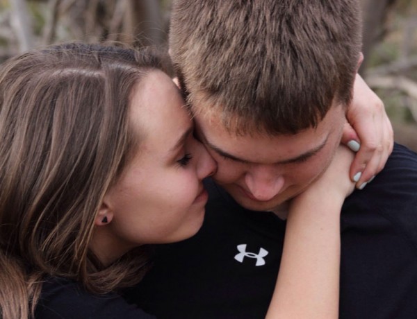 A man who is jealous looking down while his girlfriend tries to reassure him.