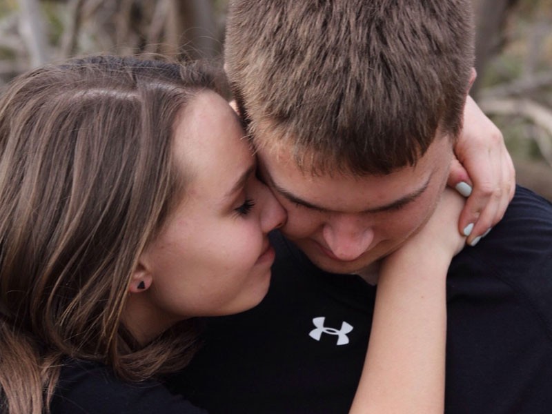 A man who is jealous looking down while his girlfriend tries to reassure him.