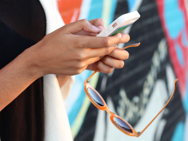 A woman sending an online dating first message while outside with sunglasses.