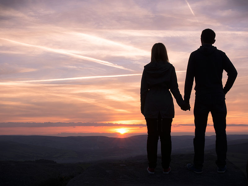 A couple having relationship issues holding hands and looking at the sunset together.