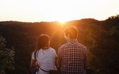 A couple on a first date asking each other first date questions while sitting in front of a sunset.