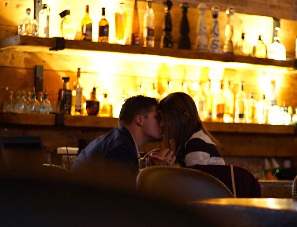 Two people kissing while sitting at the bar.