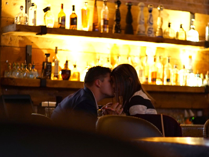 Two people kissing while sitting at the bar.