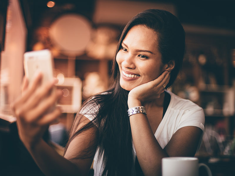 A woman who learned how to get a good profile photo taking a selfie of herself in a coffee shop.