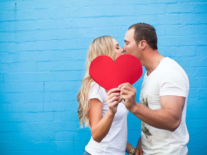 Una pareja siguiendo la línea de tiempo de una nueva relación besándose y sosteniendo un corazón.