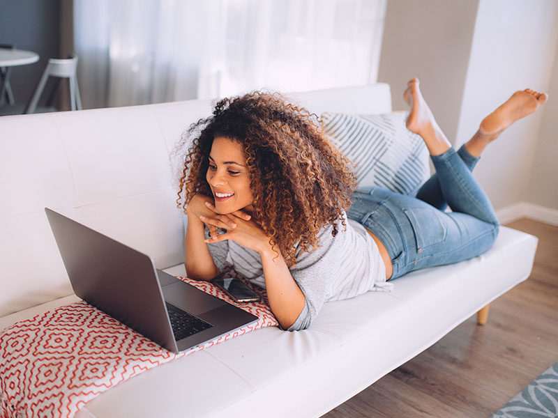 A woman on her couch typing out these online dating questions to the guy she's chatting with and laughing.