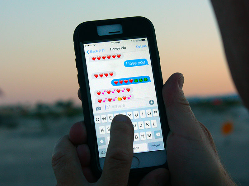 A couple in a long distance relationship texting hearts and emojis on a phone.