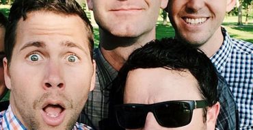 A group of men in their 30s smiling and joking together.