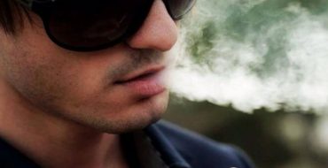 A bad boy with sunglasses on smoking a cigarette.