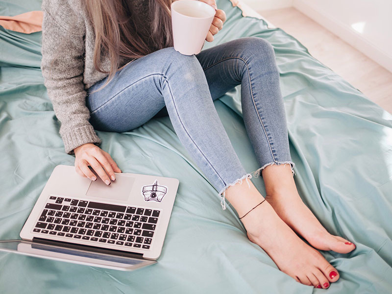 A woman filling out her online dating profile description in bed while drinking coffee.