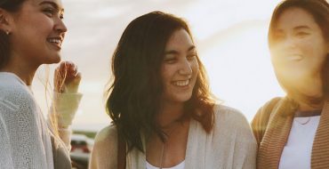 A group of sisters--oldest, middle, youngest-laughing together on a beach.