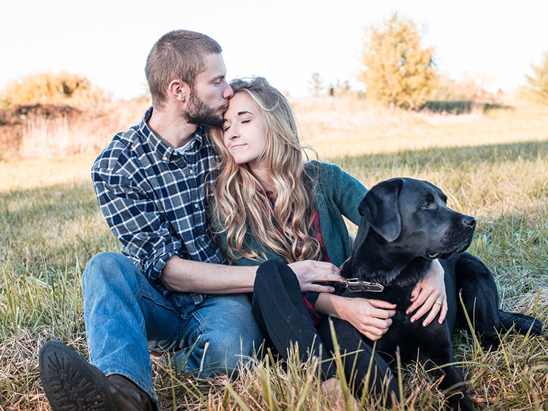 A couple rural dating in a small town kissing in a field with their dog.