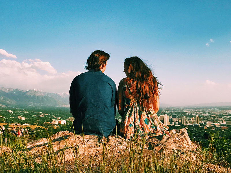 Una pareja sentada en la cima de una montaña que escuchó estos consejos de conversación para la primera cita teniendo una gran primera cita.