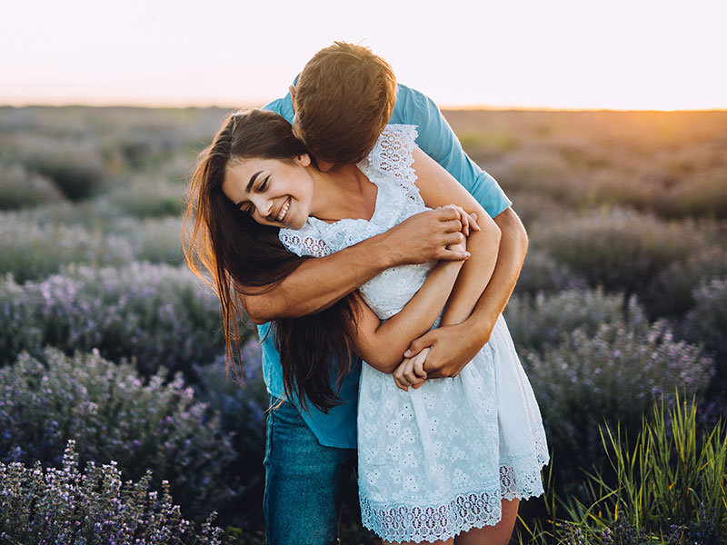 A women who learned these dating tips for women from men hugging her boyfriend and laughing in a field of flowers.