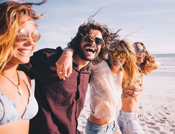 A group of highly successful singles laughing on a beach while they live the single life feeling confident in themselves.