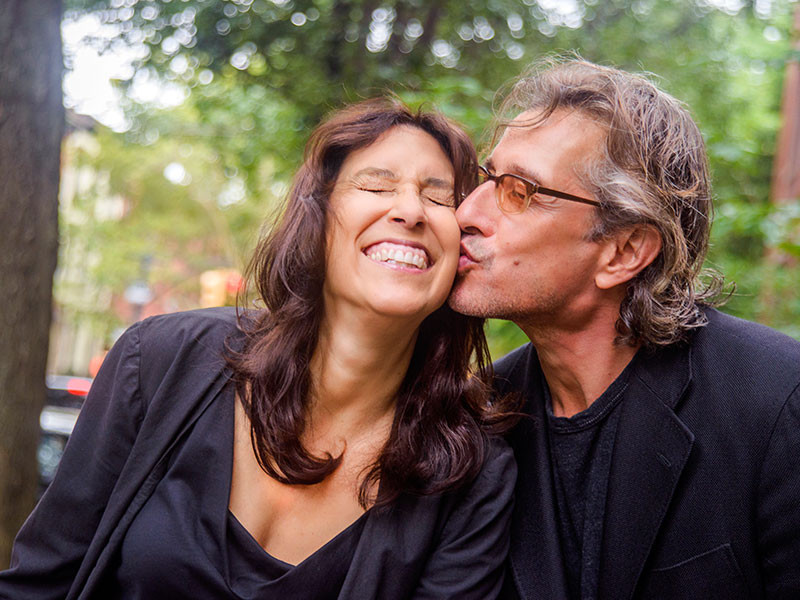 A woman who's dating a divorced man smiling as she gets a kiss on the cheek from him.