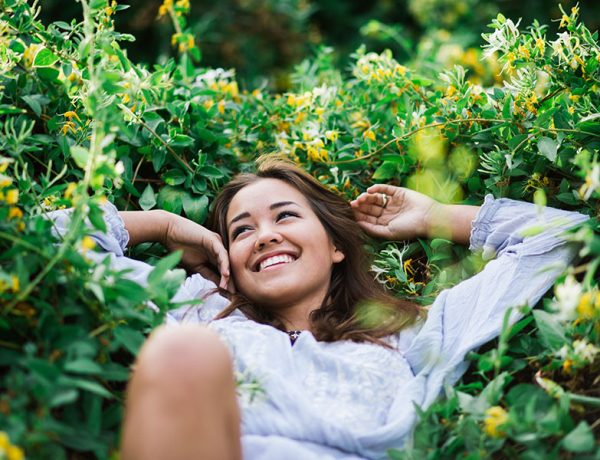 A woman who got over being unlucky in love, laughing in a pile of flowers and grass because now she's happy.
