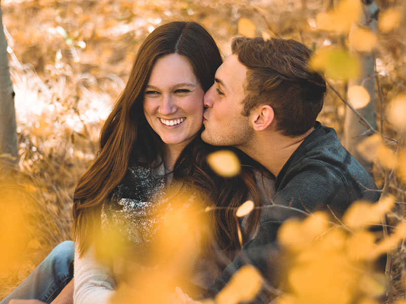 A woman who paid attention to these signs that he likes you and is now laughing in the fall leaves while the guy she likes kisses her cheek.