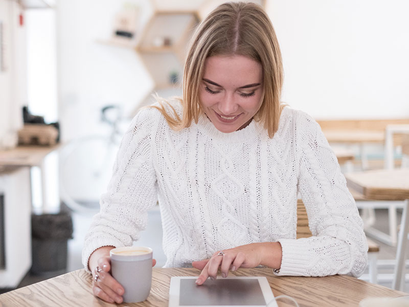 A woman reading pof headlines for men while drinking coffee in her kitchen and trying to decide who looks interesting to talk to.