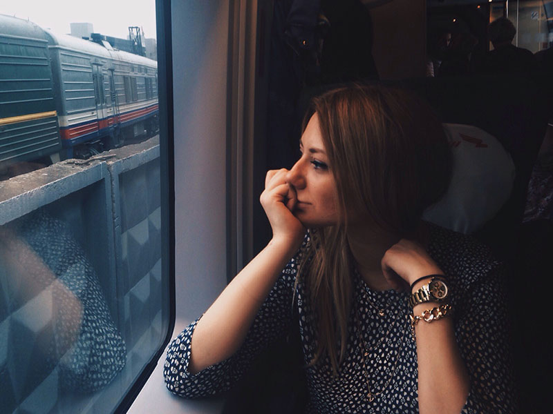 A woman who likes being single sitting on the train, smiling as she looks out the window.