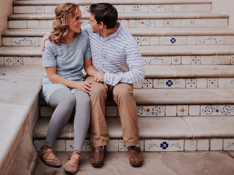 A man who is 40 and single leaning in to kiss a woman while they sit on some stairs.