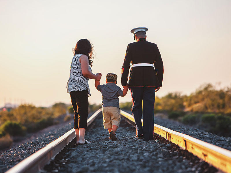 A couple in the U.S. military walking down some rail road tracks with their son.