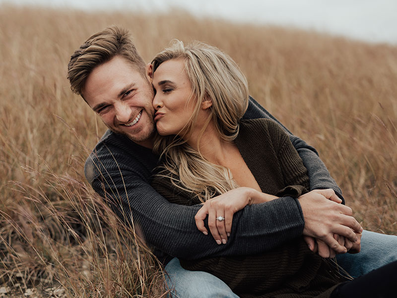 This couple kissing and laughing in a field listened to these relationship tips from happy couples.