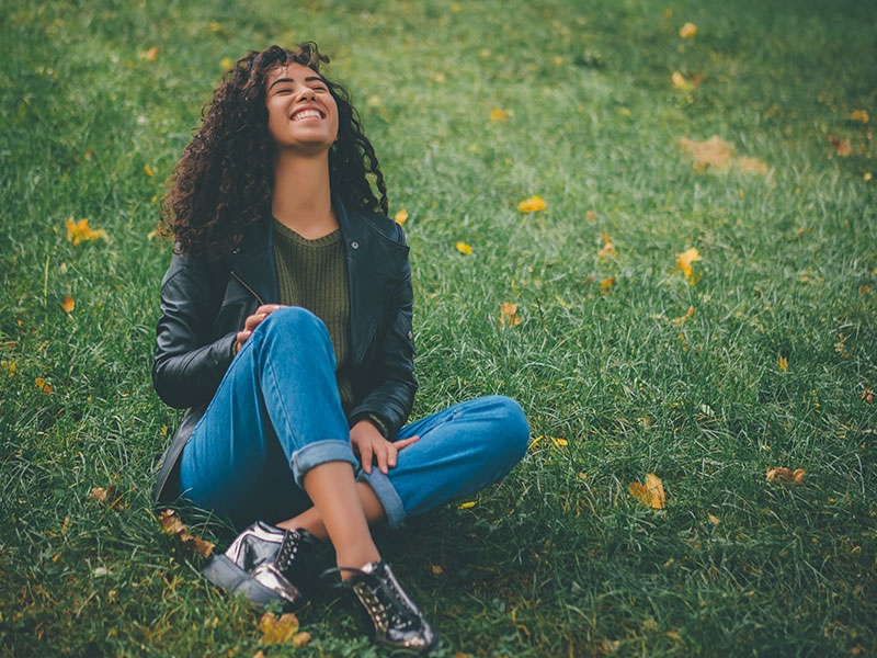 A woman who is happy living the single life smiling up at the sky why sitting on a patch of green grass.