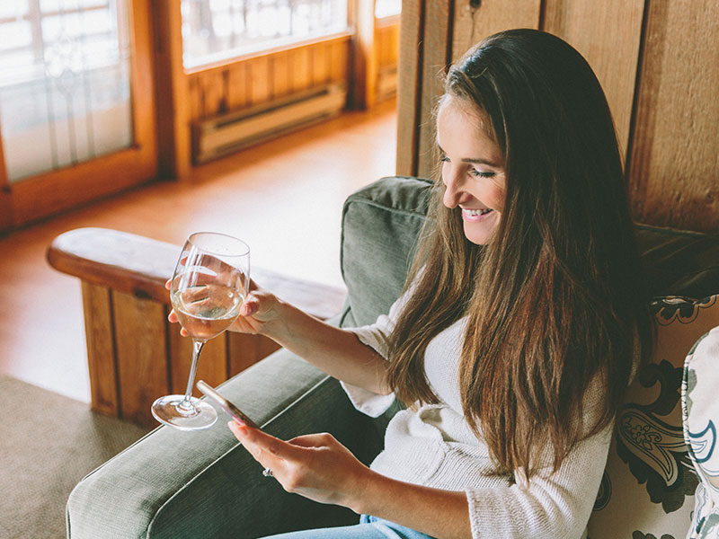 A woman who was wondering how to talk to guys online typing on her phone while drinking wine.