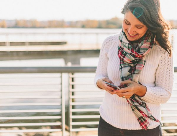 A woman on her phone outside laughing as she sets up her dating profile using these online dating tips.
