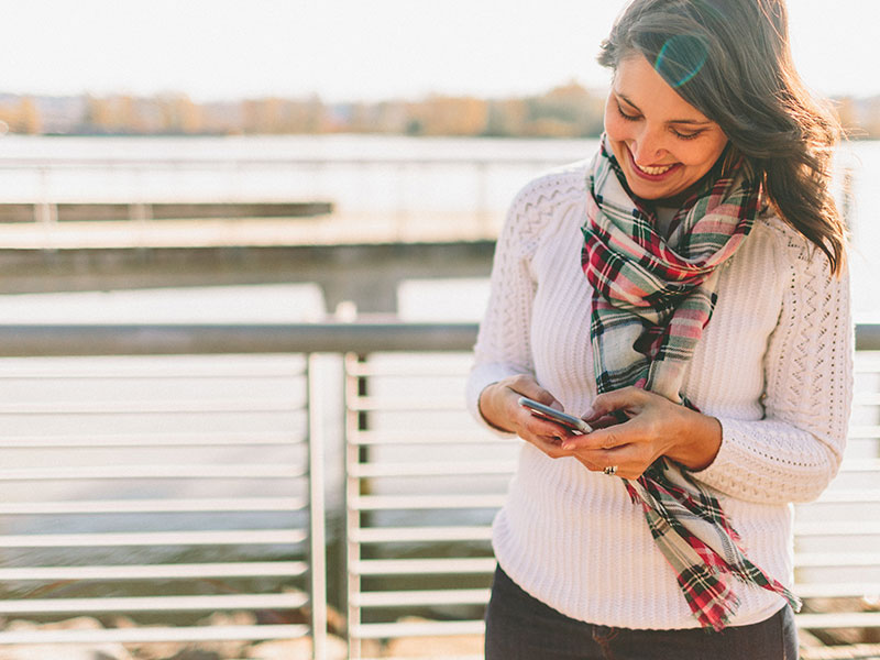 A woman on her phone outside laughing as she sets up her dating profile using these online dating tips.