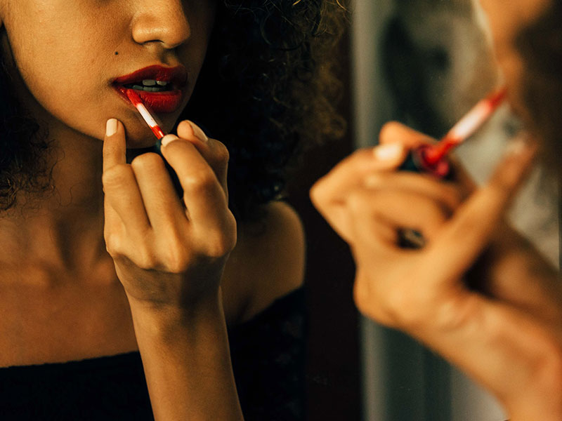 A woman applying lipstick and thinking about flirting tips.