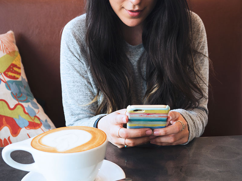 A woman taking these dating profile tips and updating her dating profile on her phone at a coffee shop.