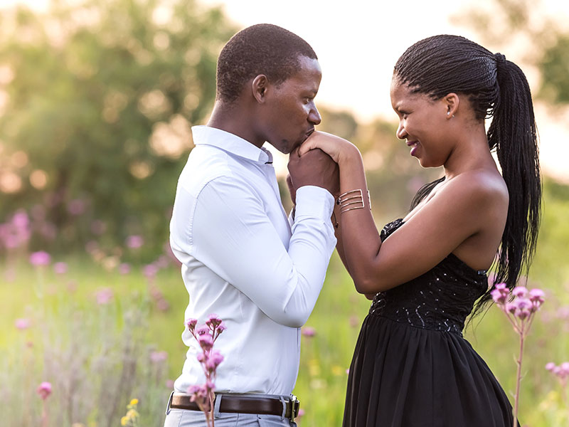 A man holding the hands of a woman who is girlfriend material in a field of flowers.