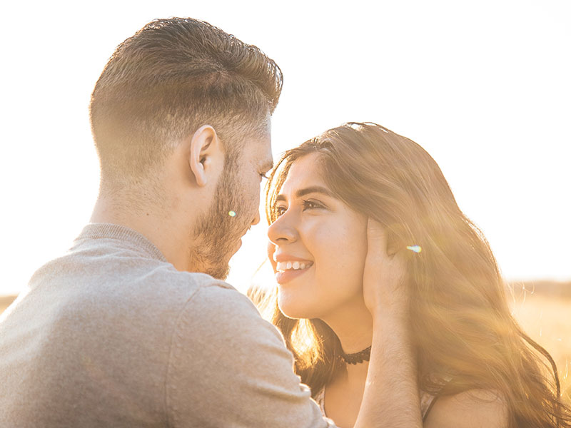 A man touching a woman's face in a field--one of turn ons for women.