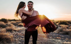 A man who was wondering does she love me, holding is girlfriend in his arms on the beach while she laughs.