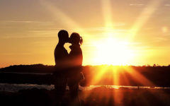 A couple standing in front of a sunset, sharing a kiss on a first date.