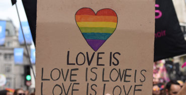 A group of people holding up a sign that says love is love is love is love at a Pride parade.