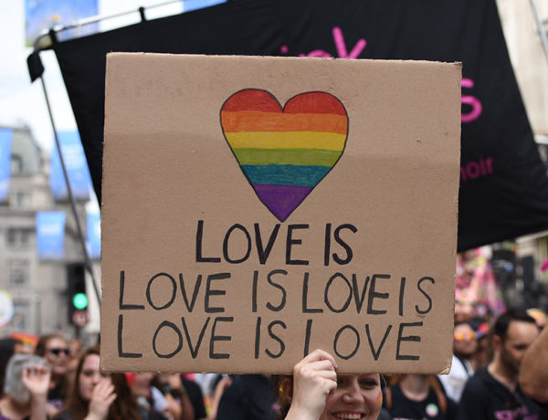 A group of people holding up a sign that says love is love is love is love at a Pride parade.