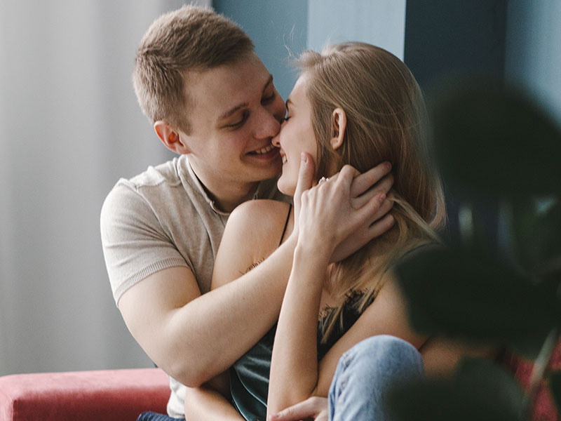 Un petit ami collant serrant sa petite amie dans ses bras tandis qu'ils sourient tous les deux et se penchent pour un baiser.