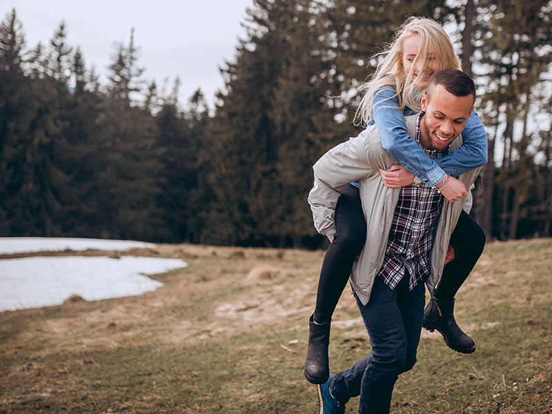 A couple that learned how to flirt laughing and smiling as the girl gets a piggy-back ride.