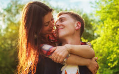 A woman who learned how to make the first move on a guy, hugging a guy from behind and flirting while he smiles.