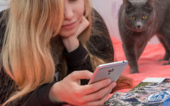 A girl looking at Tinder on her phone, trying to figure out the Tinder algorithm as her cat looks over her shoulder.
