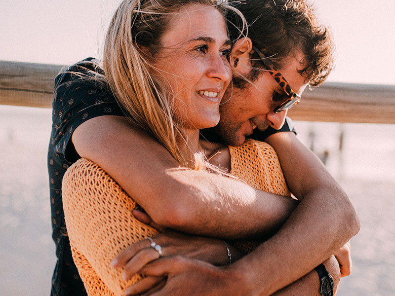 A woman who’s dating a younger man smiling while he hugs her.