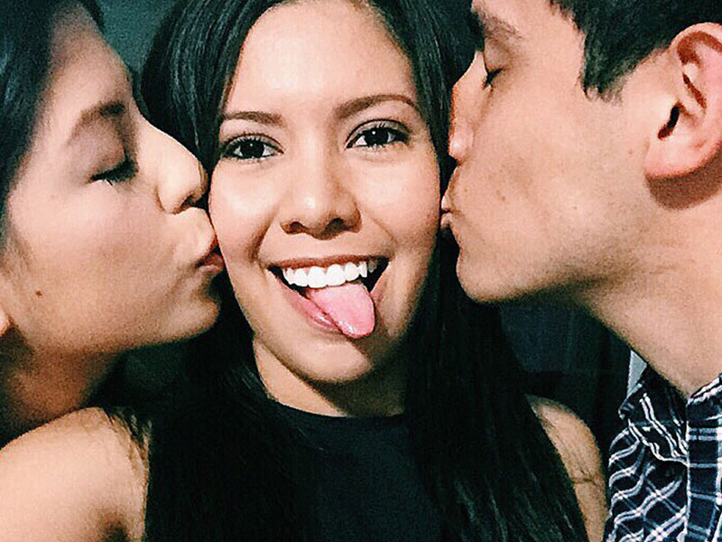 A woman who's polyamorous dating, getting her cheeks kissed by her two partners.