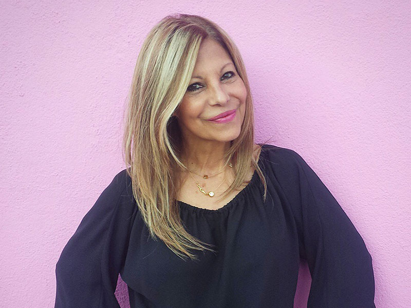 A mature women dating standing confidently and smiling in front of a pink wall.