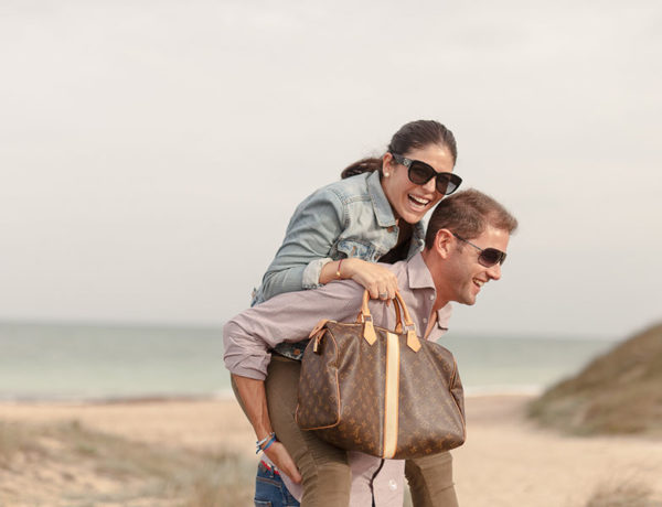 An older women dating a younger man getting a piggy back ride from her boyfriend and laughing on the beach.