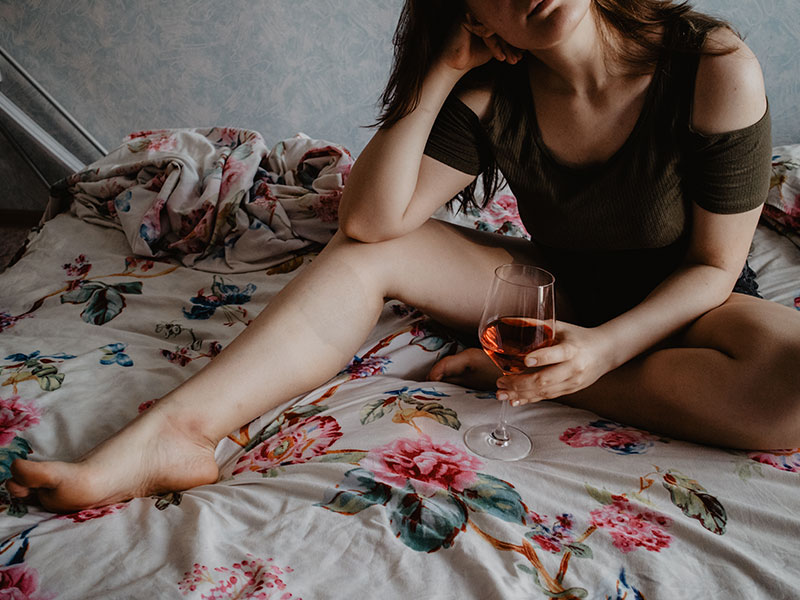 A woman who’s learning about life after divorce for women sipping wine in bed and thinking.