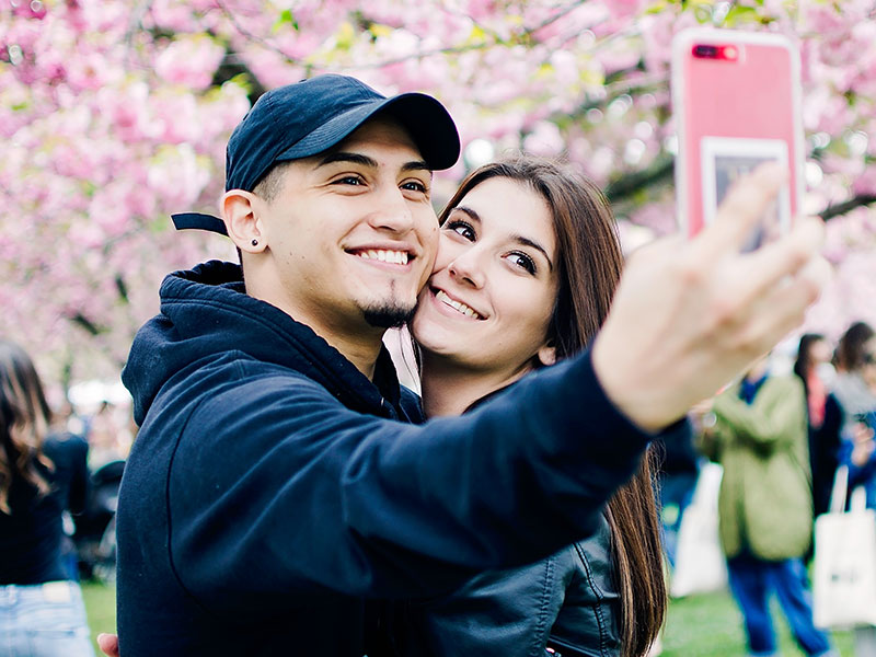 A man who said to himself, I need a girlfriend, smiling with his new girlfriend while they take a selfie at the park.