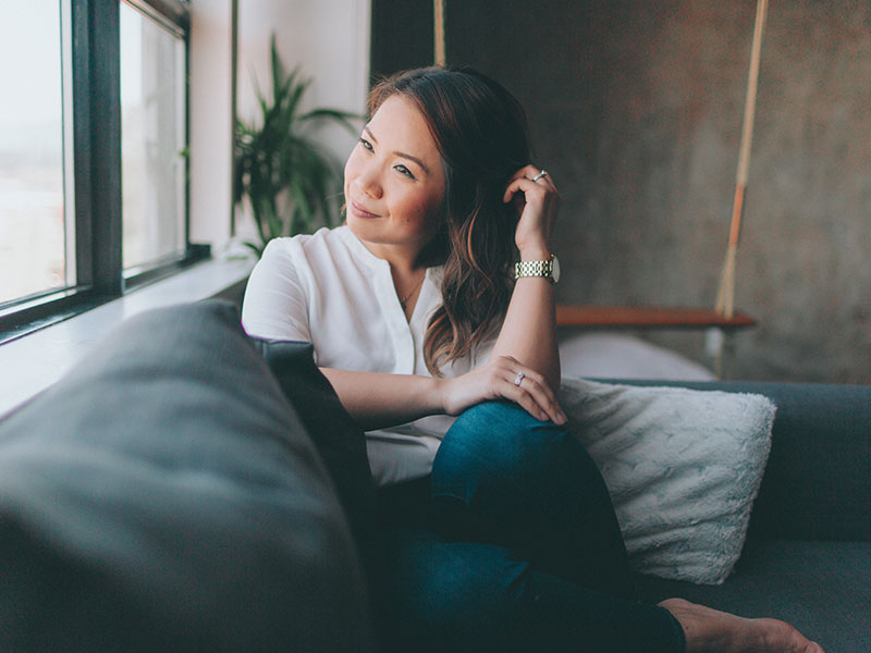 An attractive single woman over 50 sitting in a chair smiling to herself, feeling content.